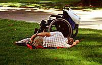 Sedia a rotelle con accanto uomo per terra. Foto copyright.